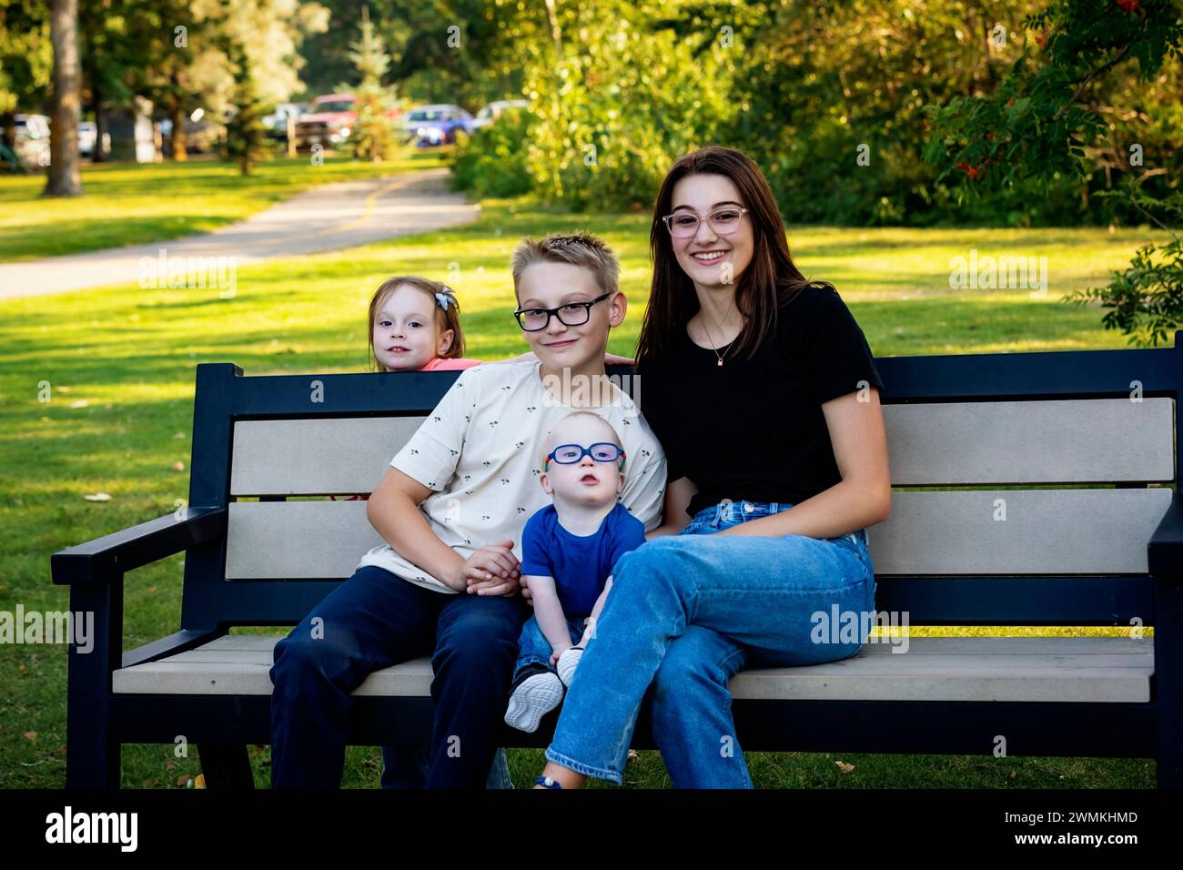 Porträt von vier Sibilings, die an einem warmen Herbstnachmittag in einem Stadtpark eine gute gemeinsame Zeit genießen und der jüngste Junge hat das Down-Syndrom Stockfoto