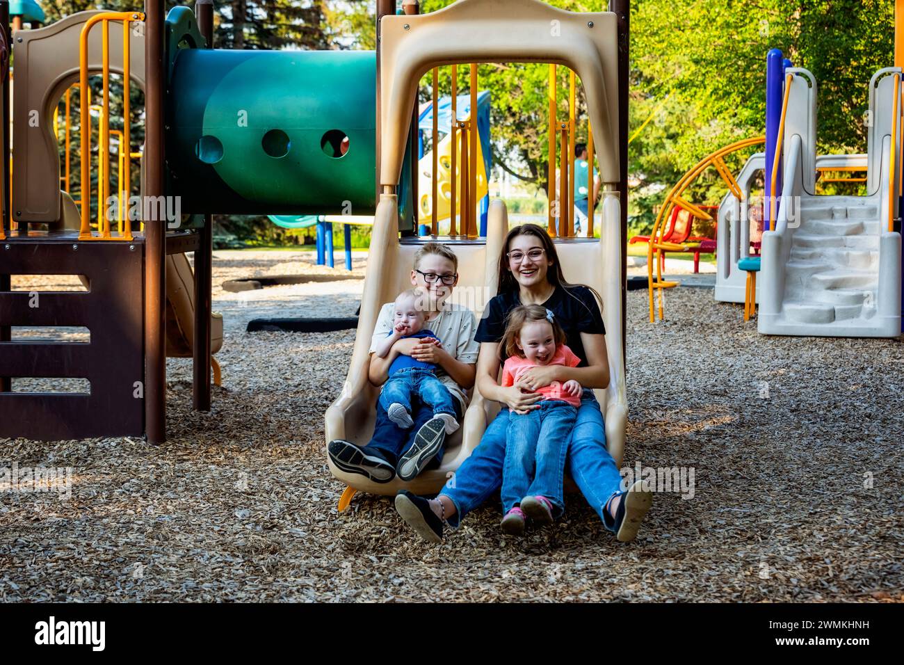 Porträt von vier Sibilings, die an einem warmen Herbstnachmittag in einem Stadtpark eine gute gemeinsame Zeit genießen und der jüngste Junge hat das Down-Syndrom Stockfoto