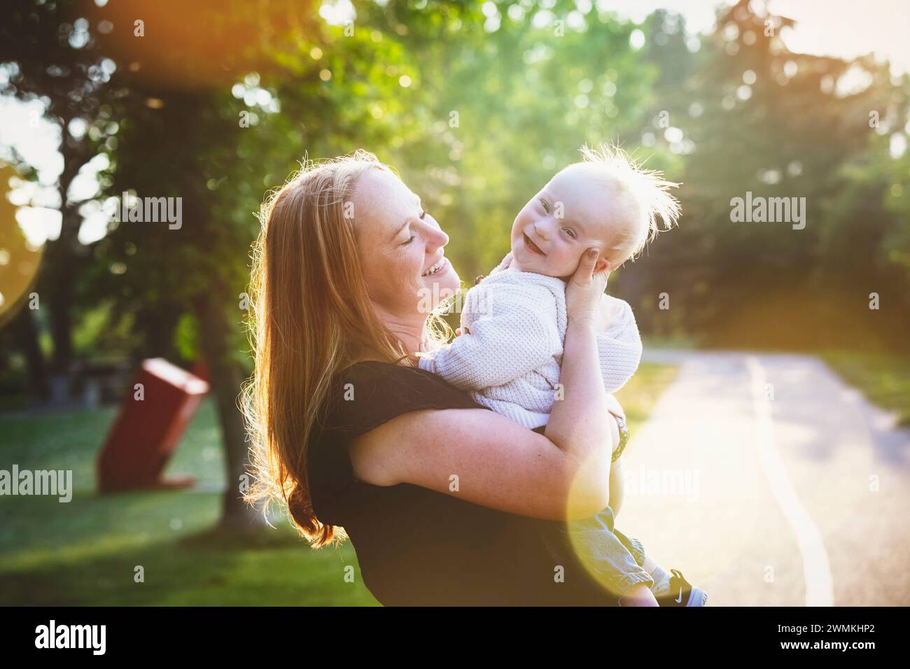 Außenporträt einer Mutter, die an einem sonnigen Herbsttag mit ihrem Sohn, der an einem Down-Syndrom leidet, in einem Stadtpark Zeit verbringt Stockfoto