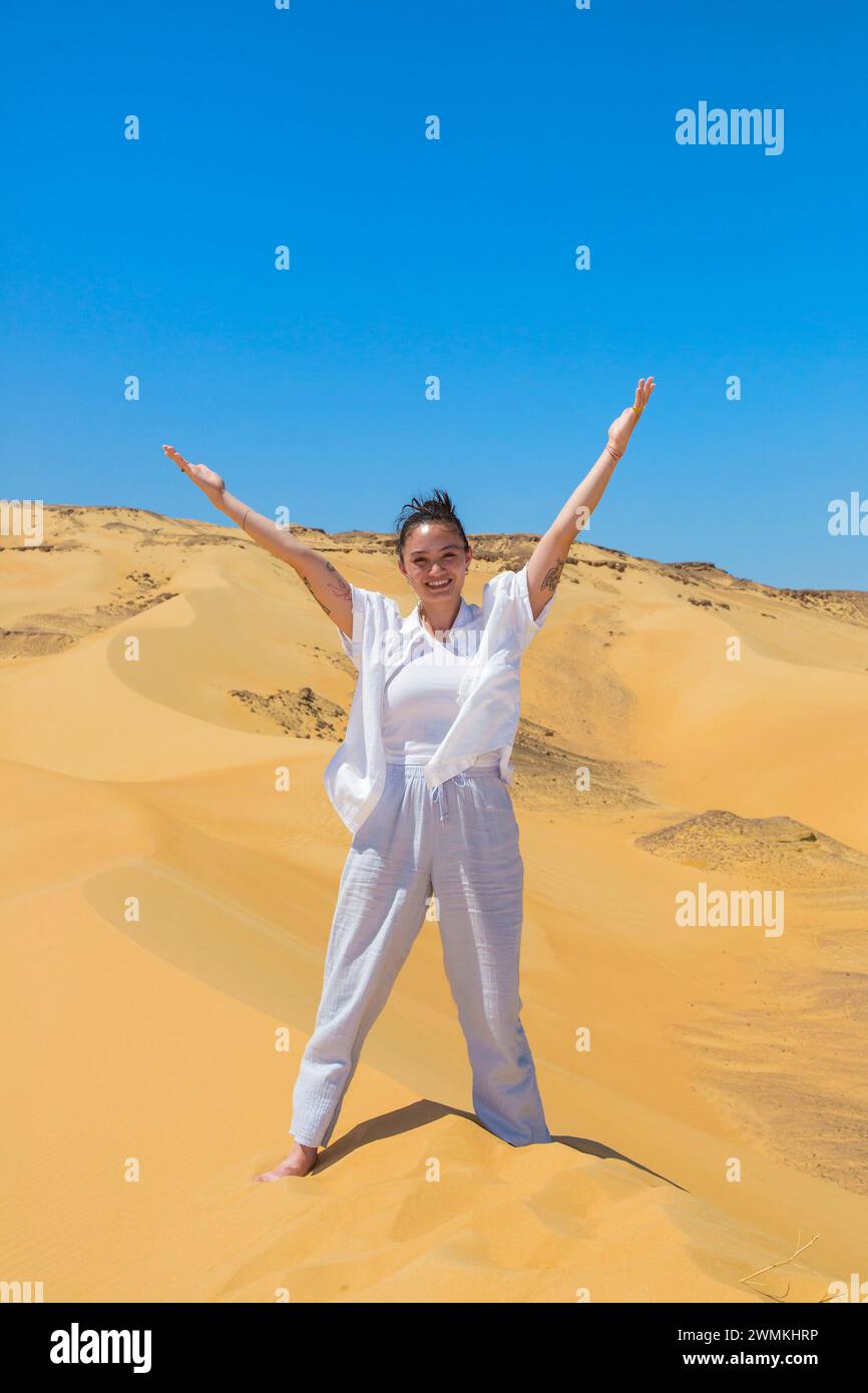Junge Frau in weißer Kleidung steht mit erhobenen Armen auf den Sanddünen des Schutzgebietes der Weißen Wüste in Ägypten Stockfoto