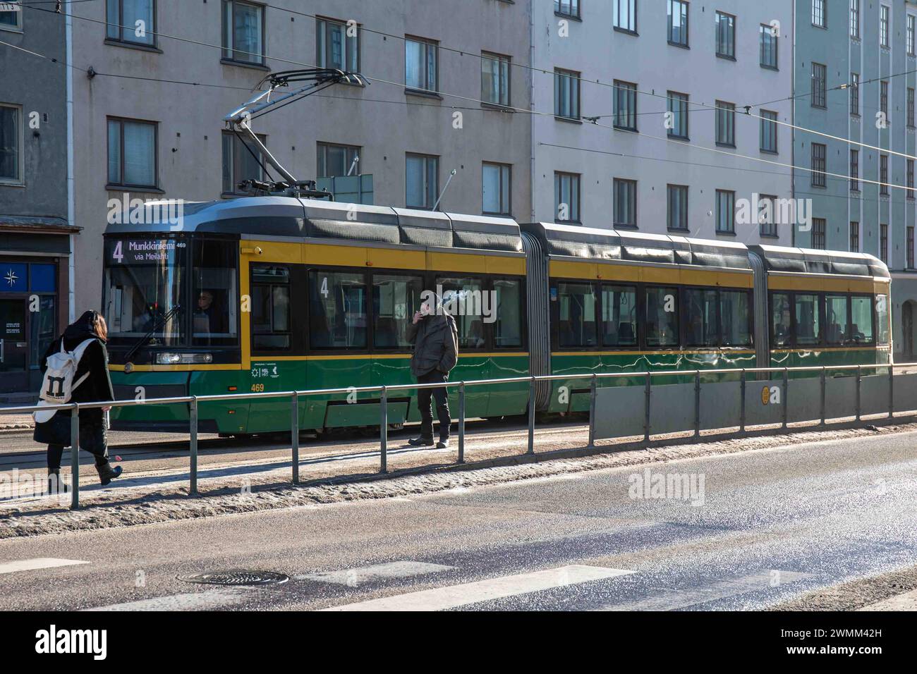 Mann raucht an der Straßenbahnhaltestelle Kansaneläkelaitos mit Straßenbahnlinie 4 im Hintergrund im Stadtteil Taka-Töölö in Helsinki, Finnland Stockfoto