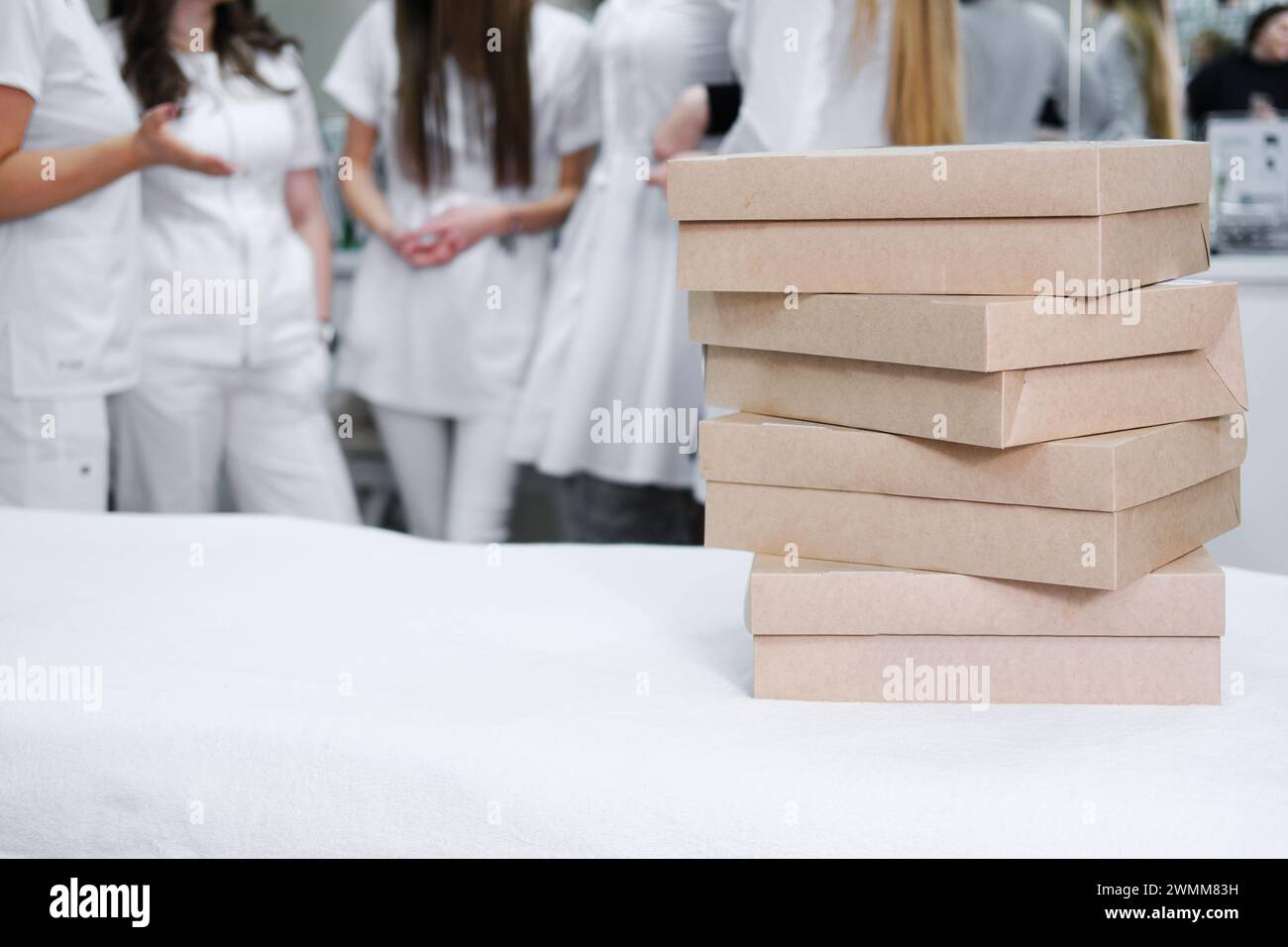 Gestapelte Catering-Boxen mit Vorspeisen auf einem Tisch im Vordergrund, mit einer Gruppe von medizinischen Fachleuten, die sich vorbereiten, im Büro Backgr zu feiern Stockfoto