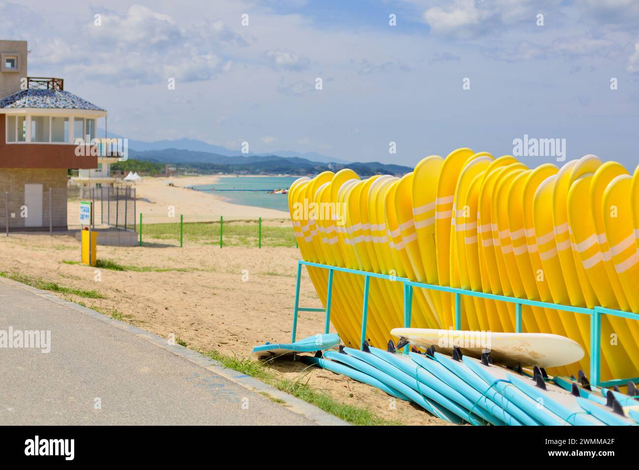 Yangyang County, Südkorea - 30. Juli 2019: Gelbe Surfbretter stehen aufrecht in einem Stift am Hyangho Beach, darunter liegen blaue Surfbretter und ein sm Stockfoto