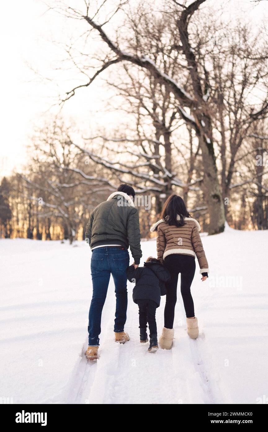 Eine glückliche Familie von drei Personen, die Hand in Hand im Schnee laufen Stockfoto