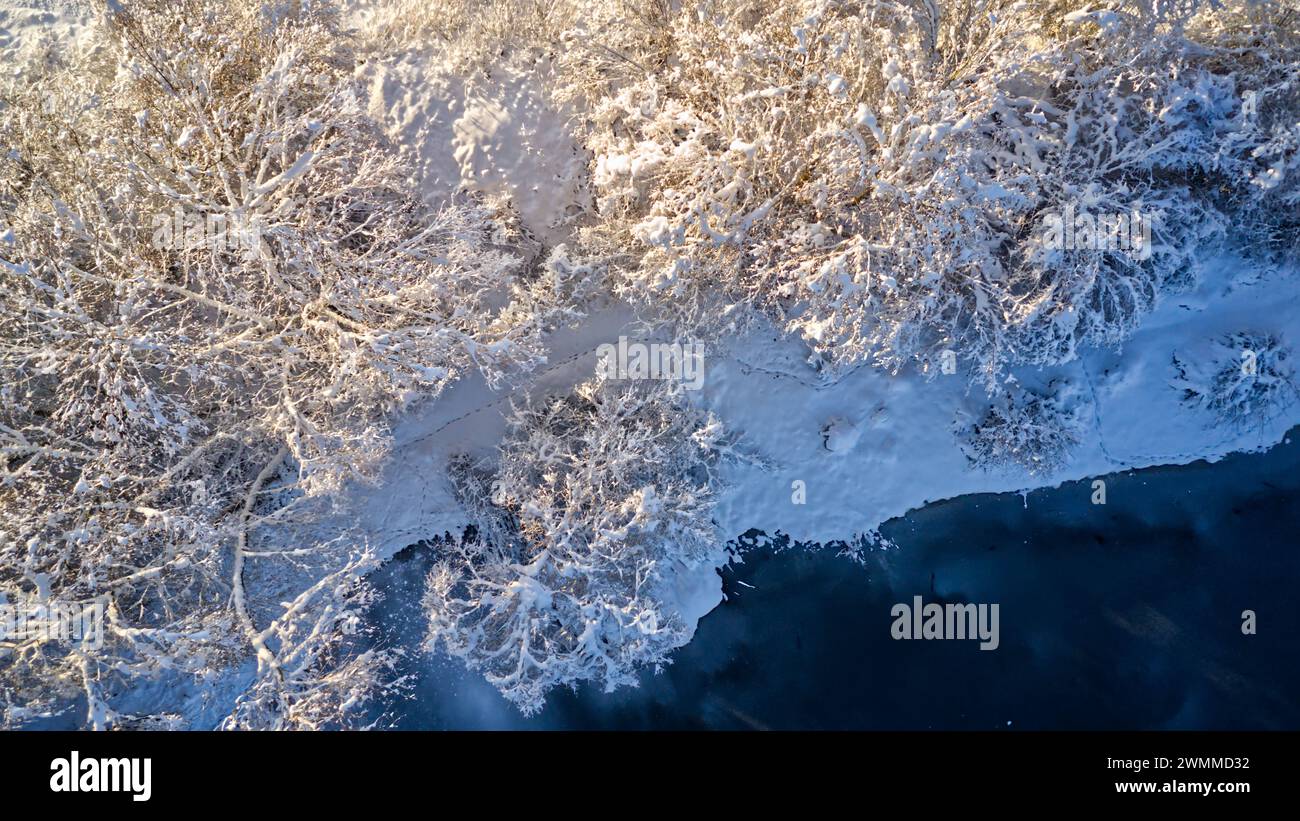 Ein schneebedeckter Wald entlang eines Flusses in einer Winterlandschaft Stockfoto