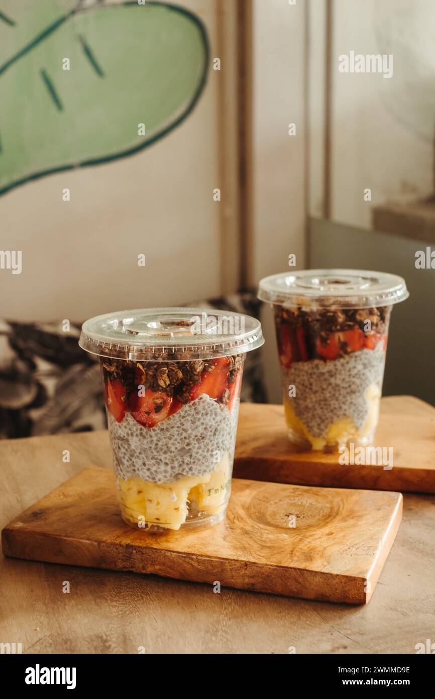 Zwei Puddings mit Obst, Müsli in einmachgläsern auf einem hölzernen Schneidebrett und ein grüner Smoothie in einer Tasse Stockfoto
