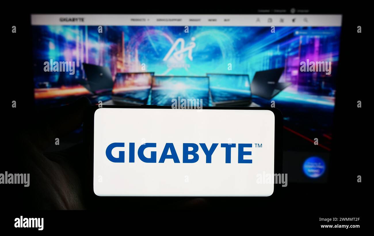 Person mit Smartphone und Logo des taiwanesischen Computerhardware-Unternehmens Gigabyte Technology vor der Website. Schwerpunkt auf dem Display des Telefons. Stockfoto