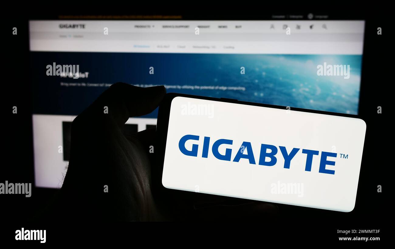 Person, die ein Mobiltelefon mit dem Logo des taiwanesischen Computerhardware-Unternehmens Gigabyte Technology vor der Webseite hält. Schwerpunkt auf dem Display des Telefons. Stockfoto