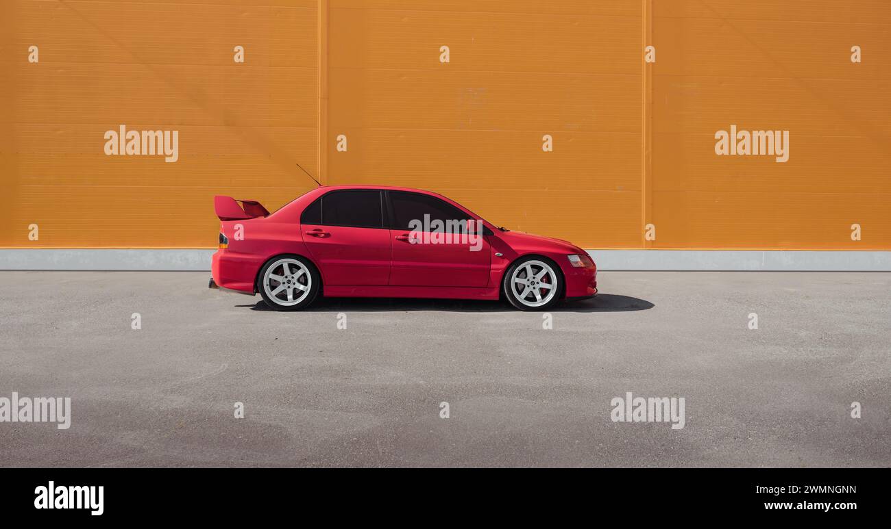 Mitsubishi Lancer Evolution IX vor der orangen Wand an einem sonnigen Tag - Seitenansicht. Stockfoto