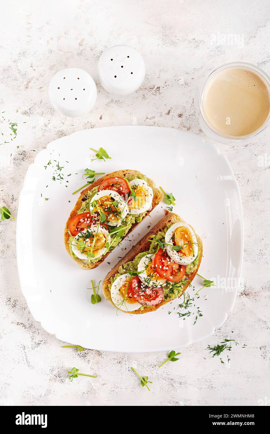 Köstlicher Toast mit Avocado, gekochtem Ei, Tomaten und Mikrogrün auf einem weißen Teller. Gesunde Ernährung, Frühstück. Keto Diätkost. Trendiges Essen. Draufsicht Stockfoto