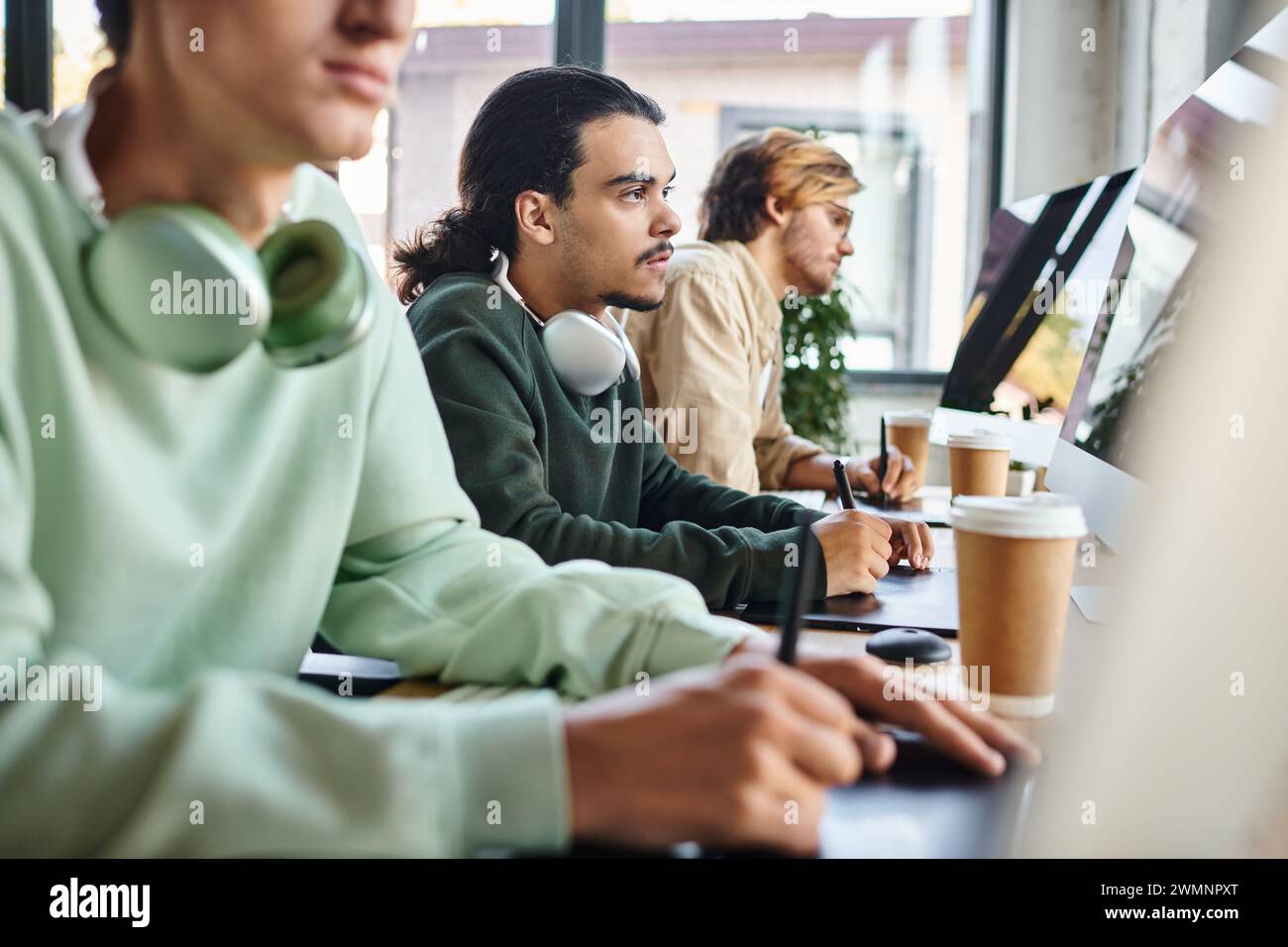 Fokussierter Mann mit Kopfhörern, der Fotos auf dem Tablet bearbeitet und den Monitor im Startup-Büro betrachtet Stockfoto