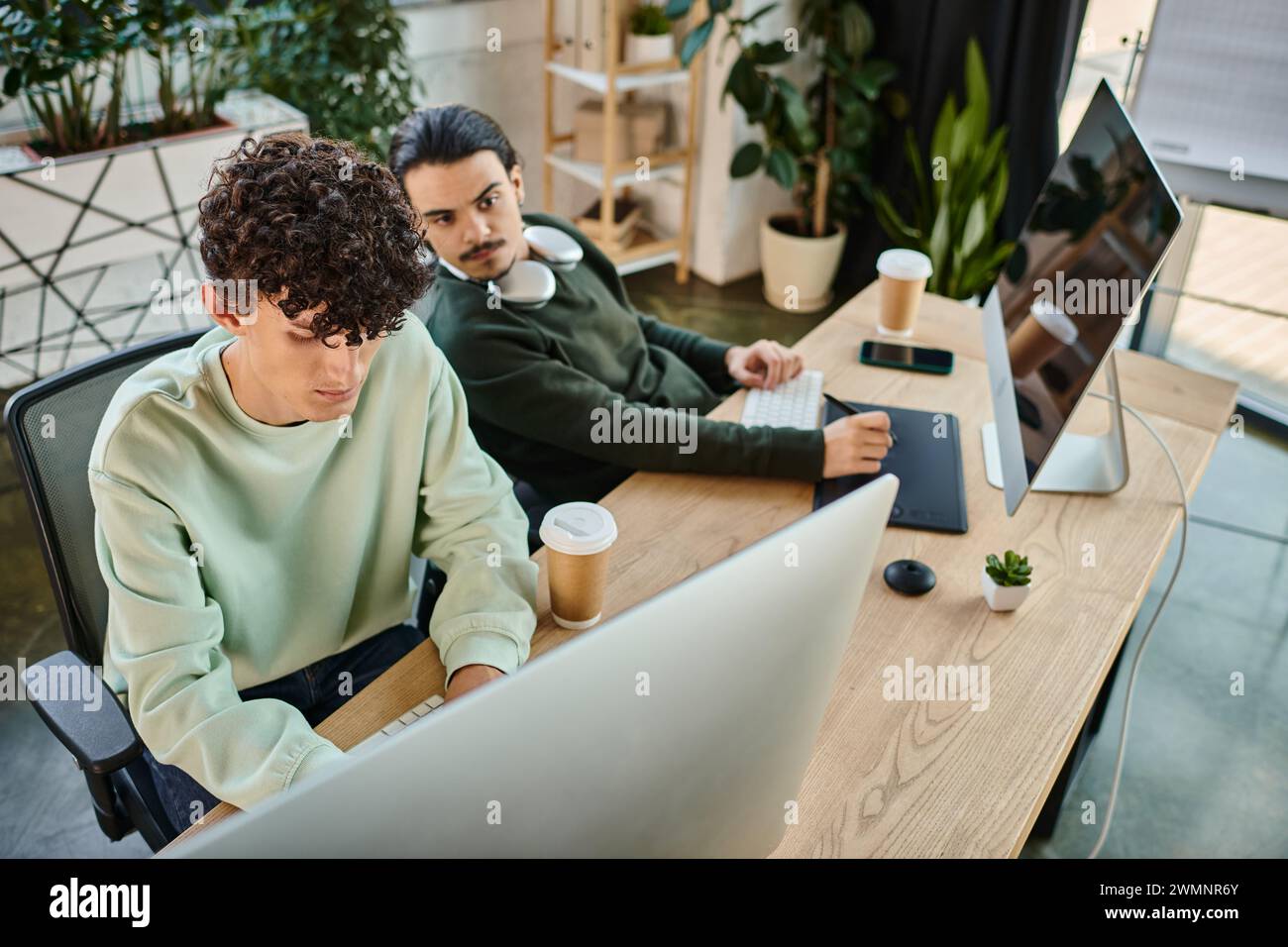 Mitarbeiter, die in einem Postproduktionsbüro eines Startup-Unternehmens an Retuschieraufgaben arbeiten, Männer in 20ern Stockfoto