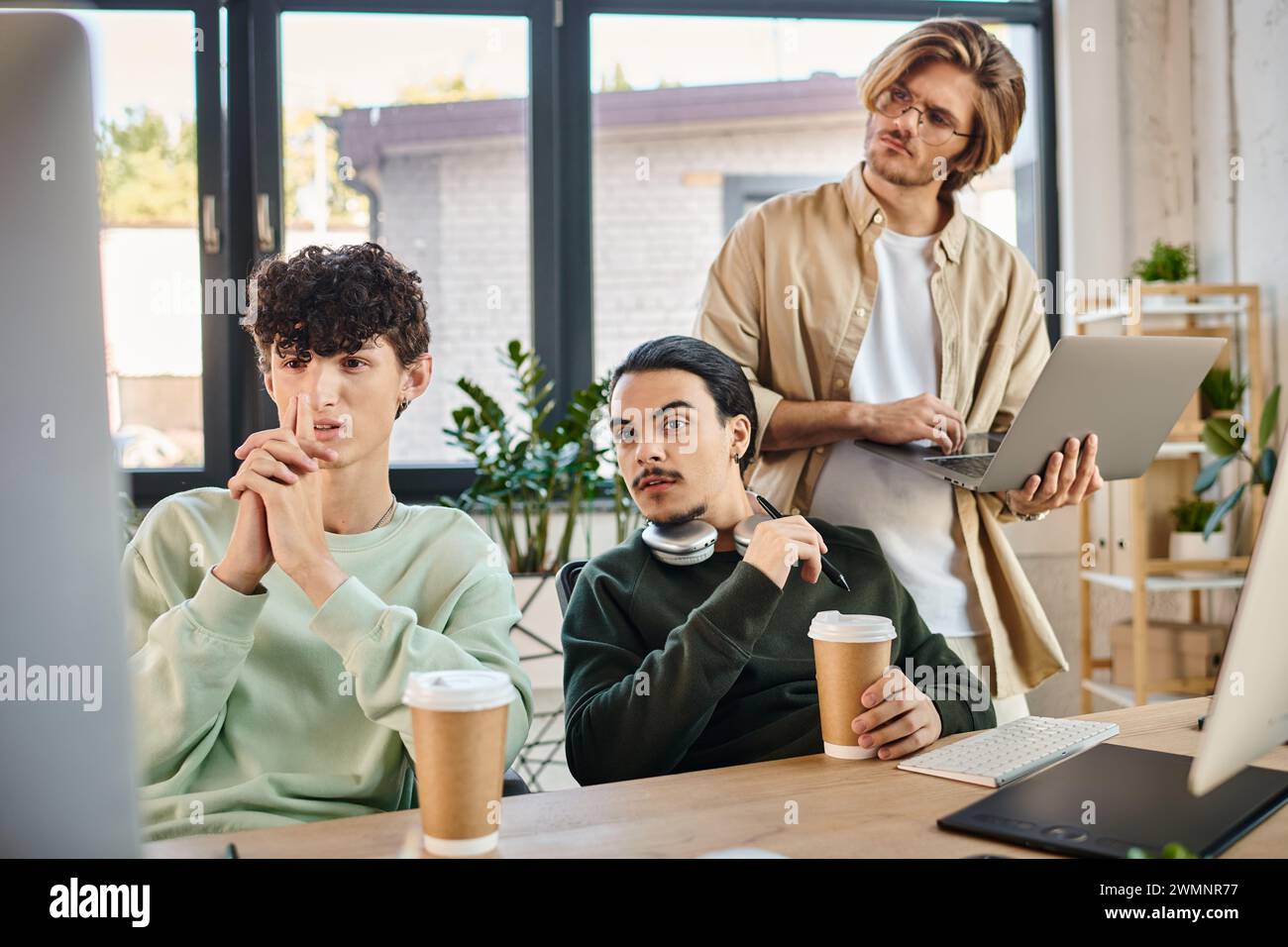 Das Postproduktionsteam junger Männer konzentrierte sich auf ein Retuschierprojekt auf Monitor in einem gut beleuchteten Büro Stockfoto