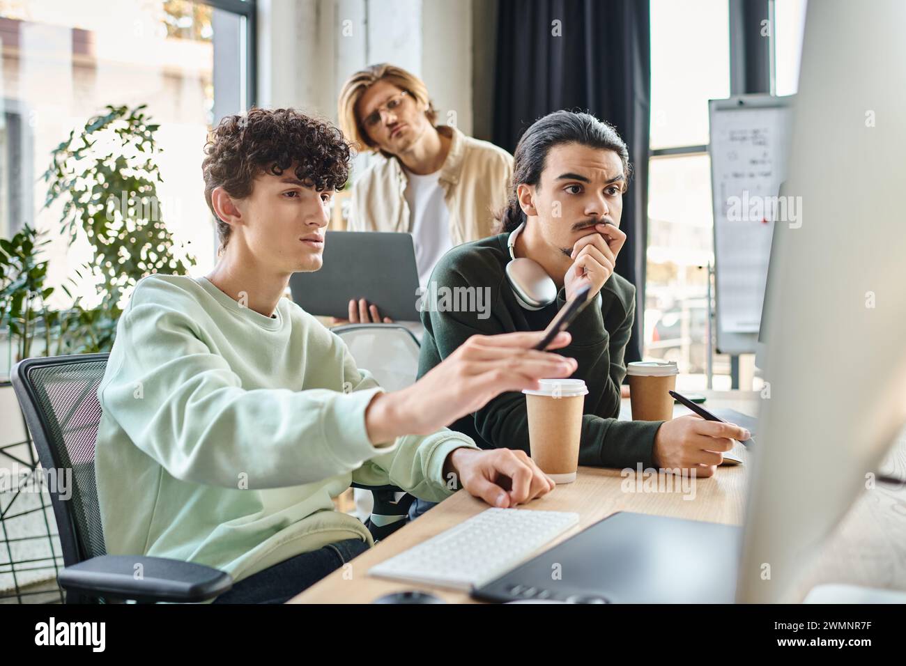 Postproduktionsteam diskutiert Retuschierprojekt auf Monitor in modernen Büros, Männer in 20ern Stockfoto
