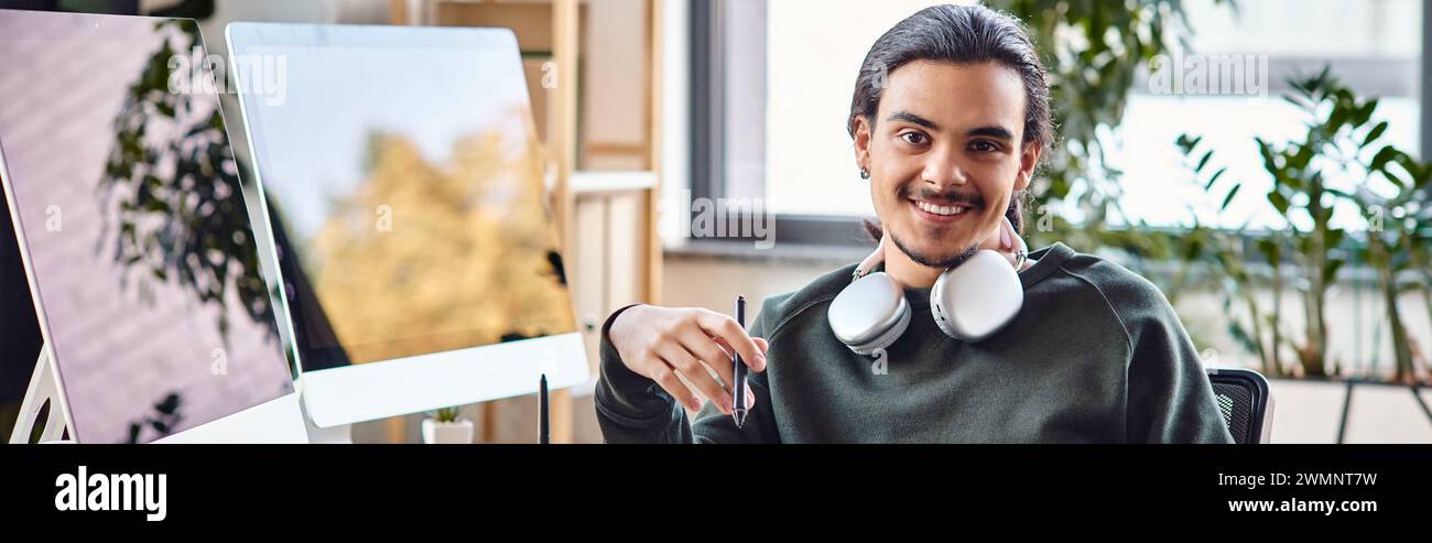 Entspannter junger Mann mit Stift, der an einem Postproduktionsarbeitsplatz des Startup lächelt, Banner Stockfoto