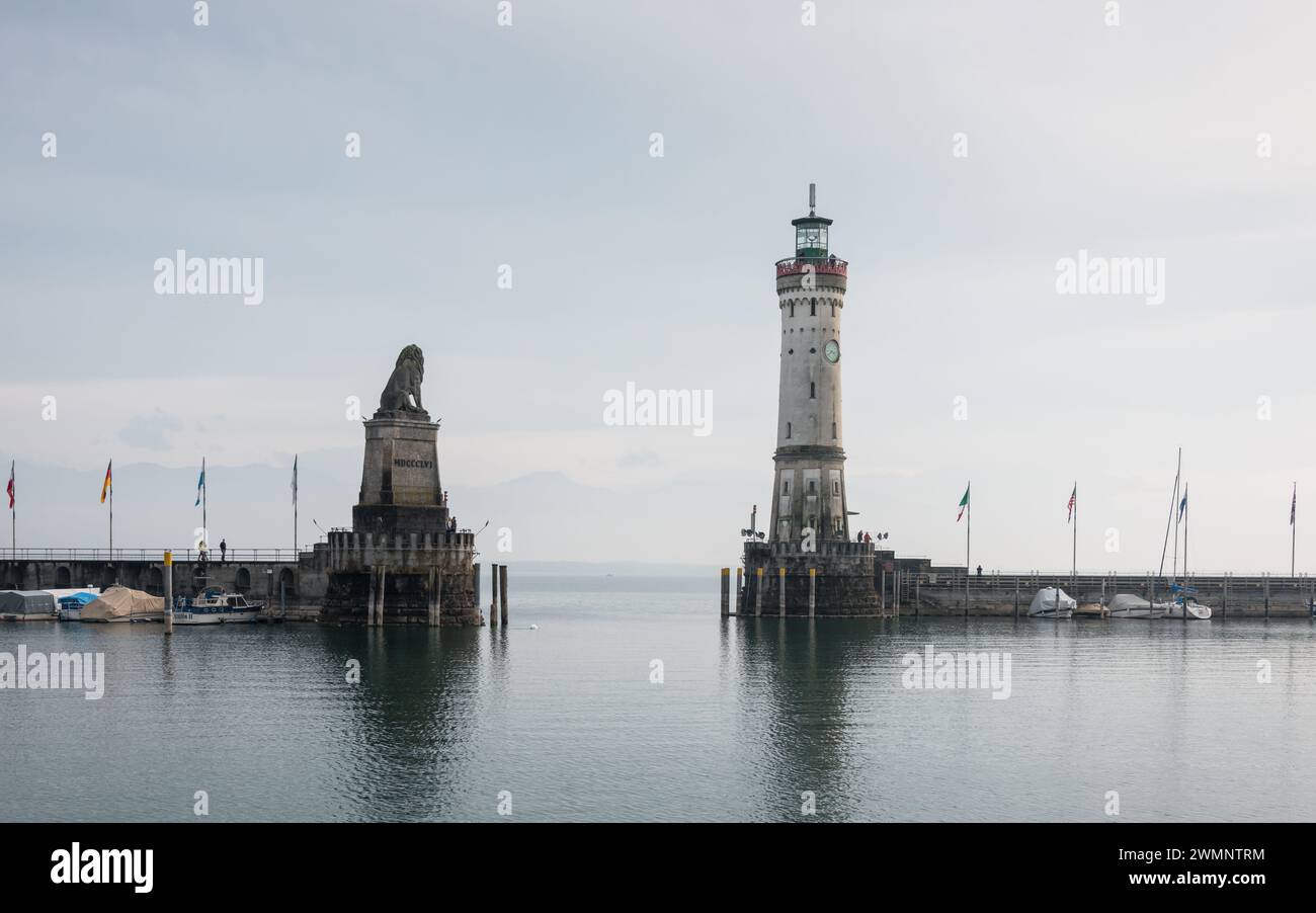 Leuchtturm und Löwenstatue am Eingang zum halb leeren Hafen an einem bewölkten Morgen. Das andere Ufer des Sees ist von Nebel bedeckt. Stockfoto