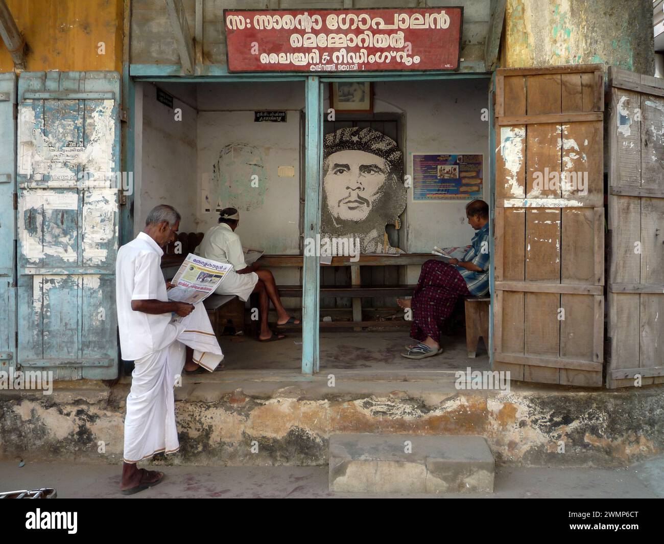 Indien, kerala, Kochi: Indische Männer lesen die Zeitung in einem öffentlichen Büro der Kommunistischen Partei Keralas mit dem Bild von Che Gevara Stockfoto