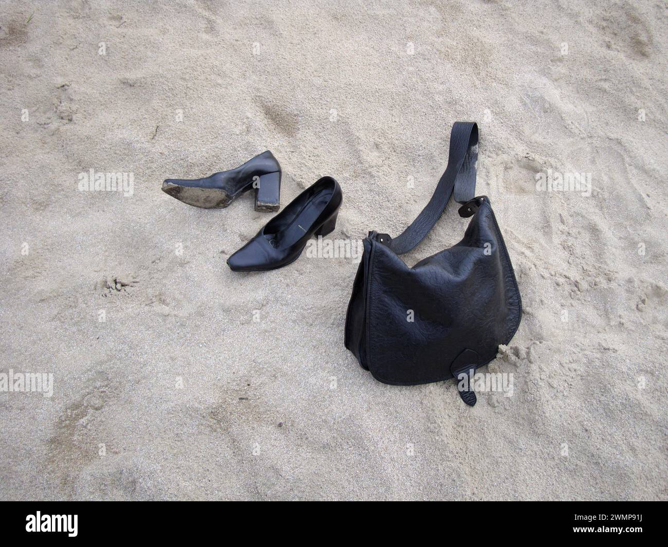 Natur-Morte. SAC à Main noir et escarpin noirs à talons carrés sur plage de Sable. Schwarze Handtasche und Schuhe mit quadratischem Absatz am Sandstrand. Stockfoto