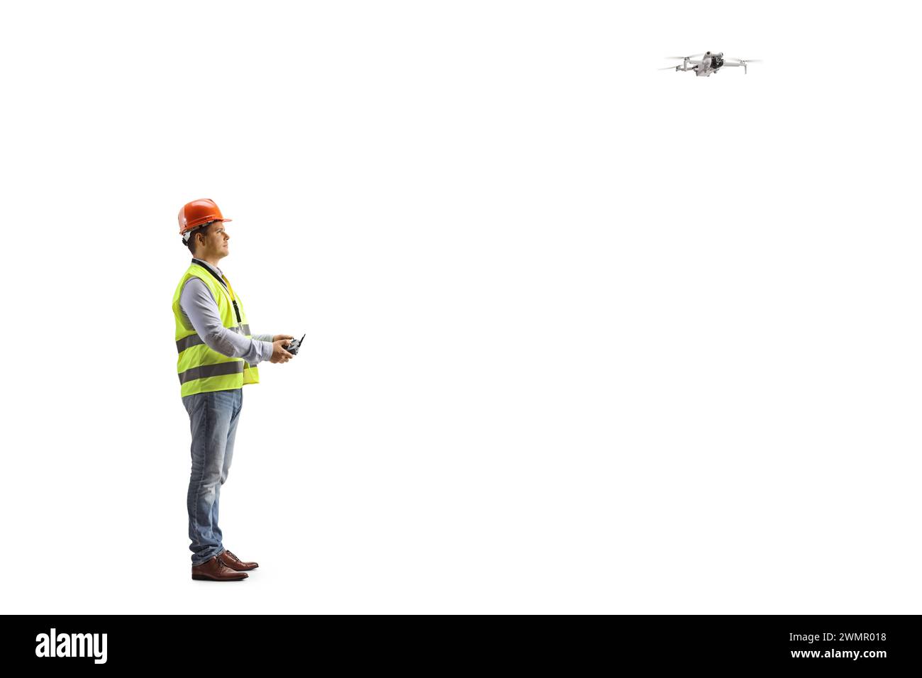 Ingenieur in einer Sicherheitsweste, die eine Drohne mit einer Fernbedienung auf weißem Hintergrund fliegt Stockfoto