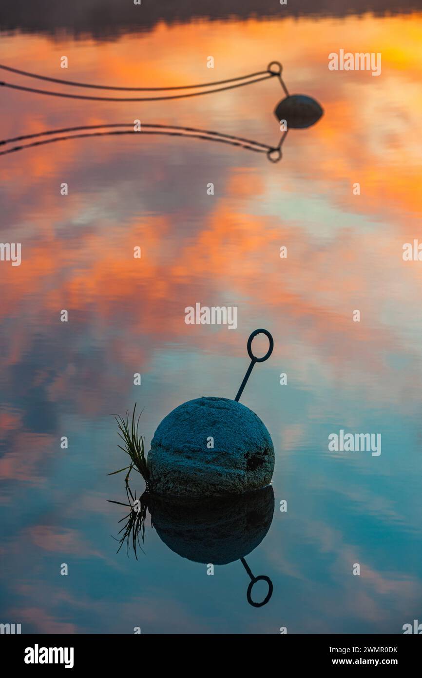 Während die Sonne über einem ruhigen See in Schweden untergeht, spiegeln sich die warmen Himmeln auf der Wasseroberfläche. Eine einsame Bojen schwimmt friedlich, gefesselt vorbei Stockfoto