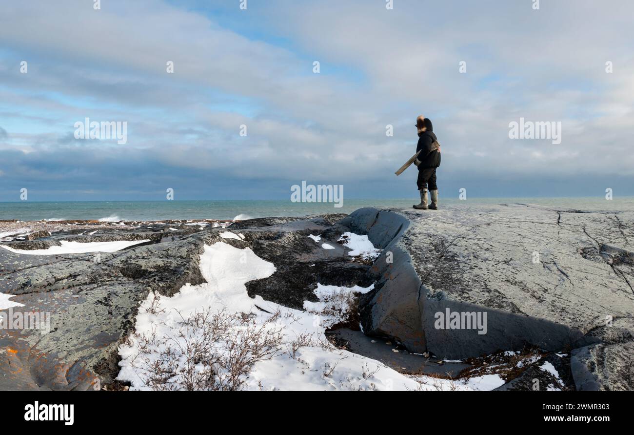 Ein bewaffneter Bärenwächter beobachtet die Küste von Hudson's Bay nach Eisbären an der historischen Stätte von Cape Merry in Churchill, Manitoba, Kanada Stockfoto