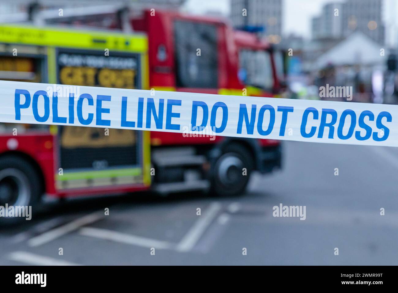 Blau-weiß-POLIZEILINIE KREUZT KEIN Band mit einem Feuerwehrauto im Hintergrund am Ort eines Brandes in Großbritannien. Foto: Amanda Rose/Alamy Stockfoto