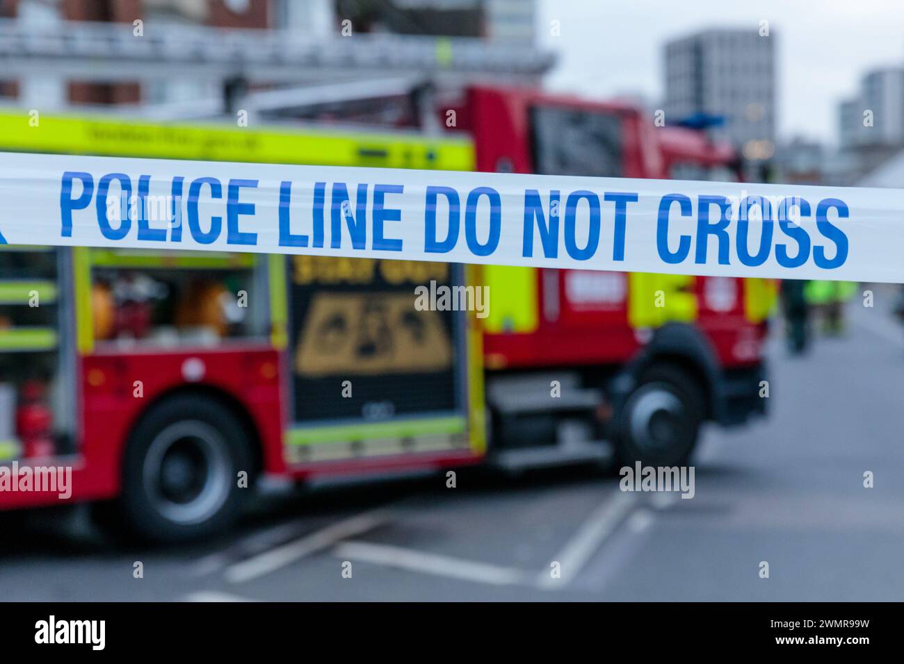 Blau-weiß-POLIZEILINIE KREUZT KEIN Band mit einem Feuerwehrauto im Hintergrund am Ort eines Brandes in Großbritannien. Foto: Amanda Rose/Alamy Stockfoto