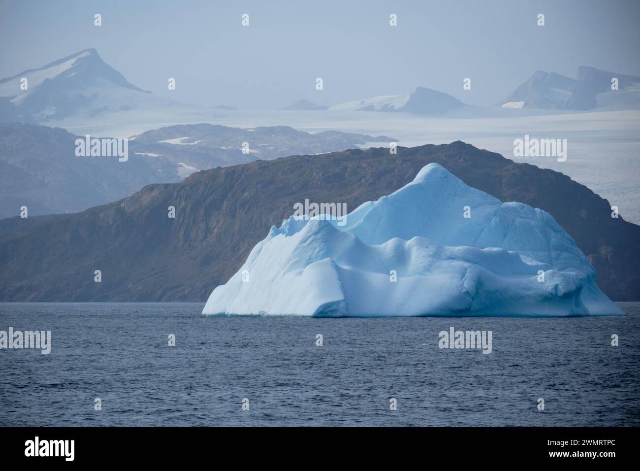 Zarte türkisfarbene Eisbergschwaden an der Küste Ostgrönlands. Im Hintergrund befinden sich die Berge und Gletscher des Festlandes. Stockfoto