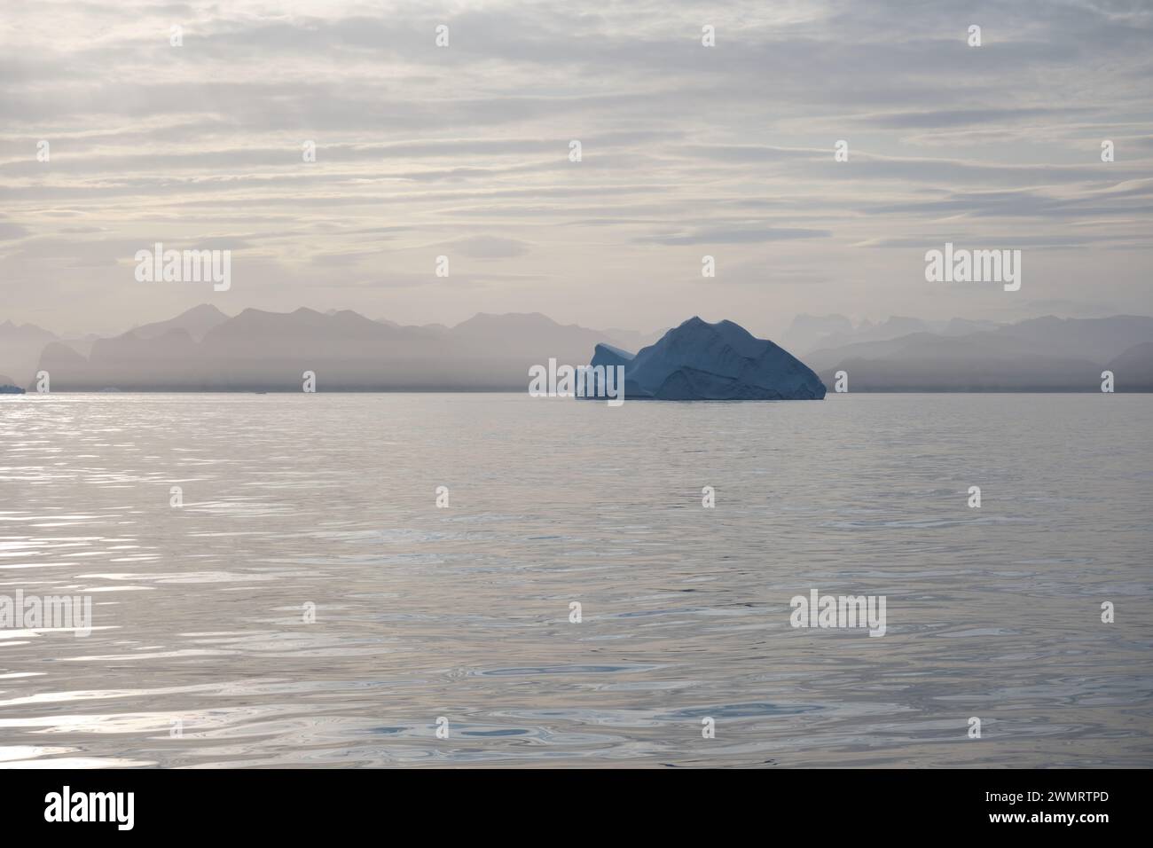 Eisberg schweben im goldenen Meer, während die Sonne untergeht und goldenes Licht über die Berge und das Eis Ostgrönlands verbreitet. Stockfoto