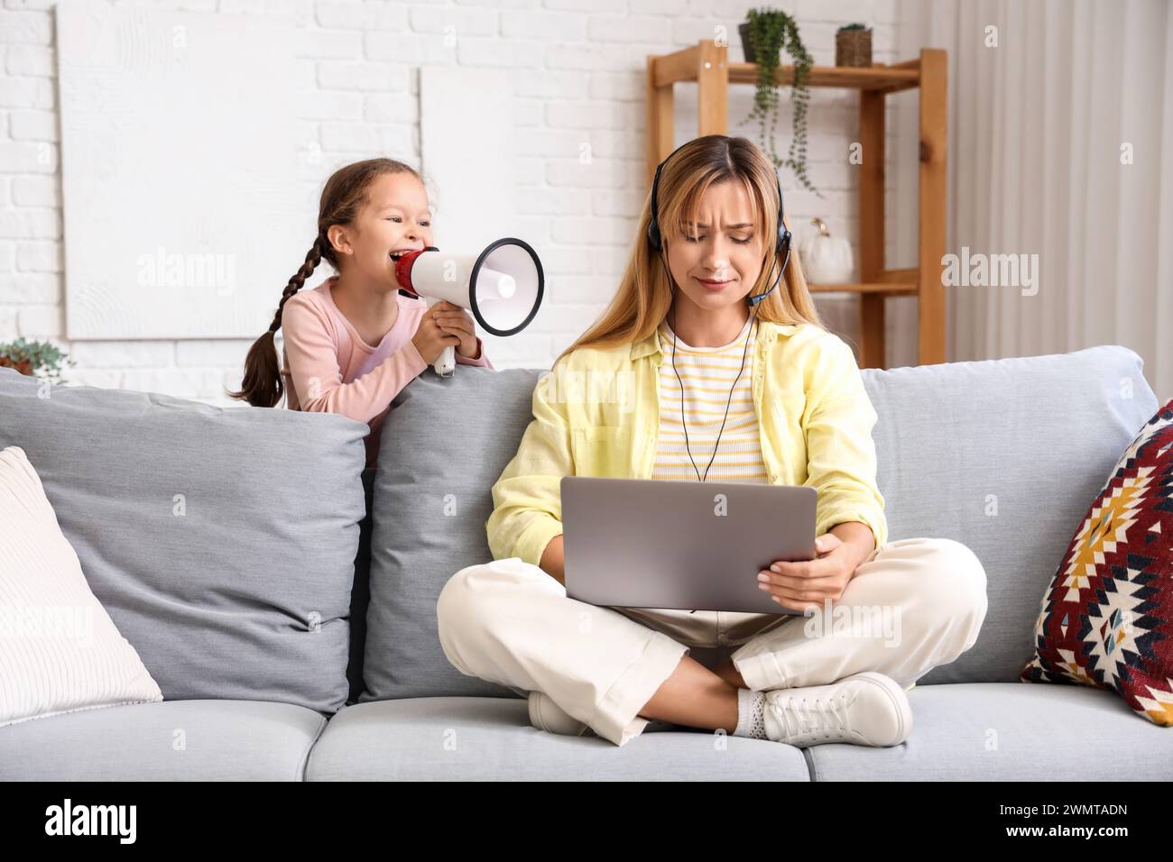 Die arbeitende junge Frau war gestresst, dass ihre laute kleine Tochter zu Hause in Megaphon brüllt Stockfoto