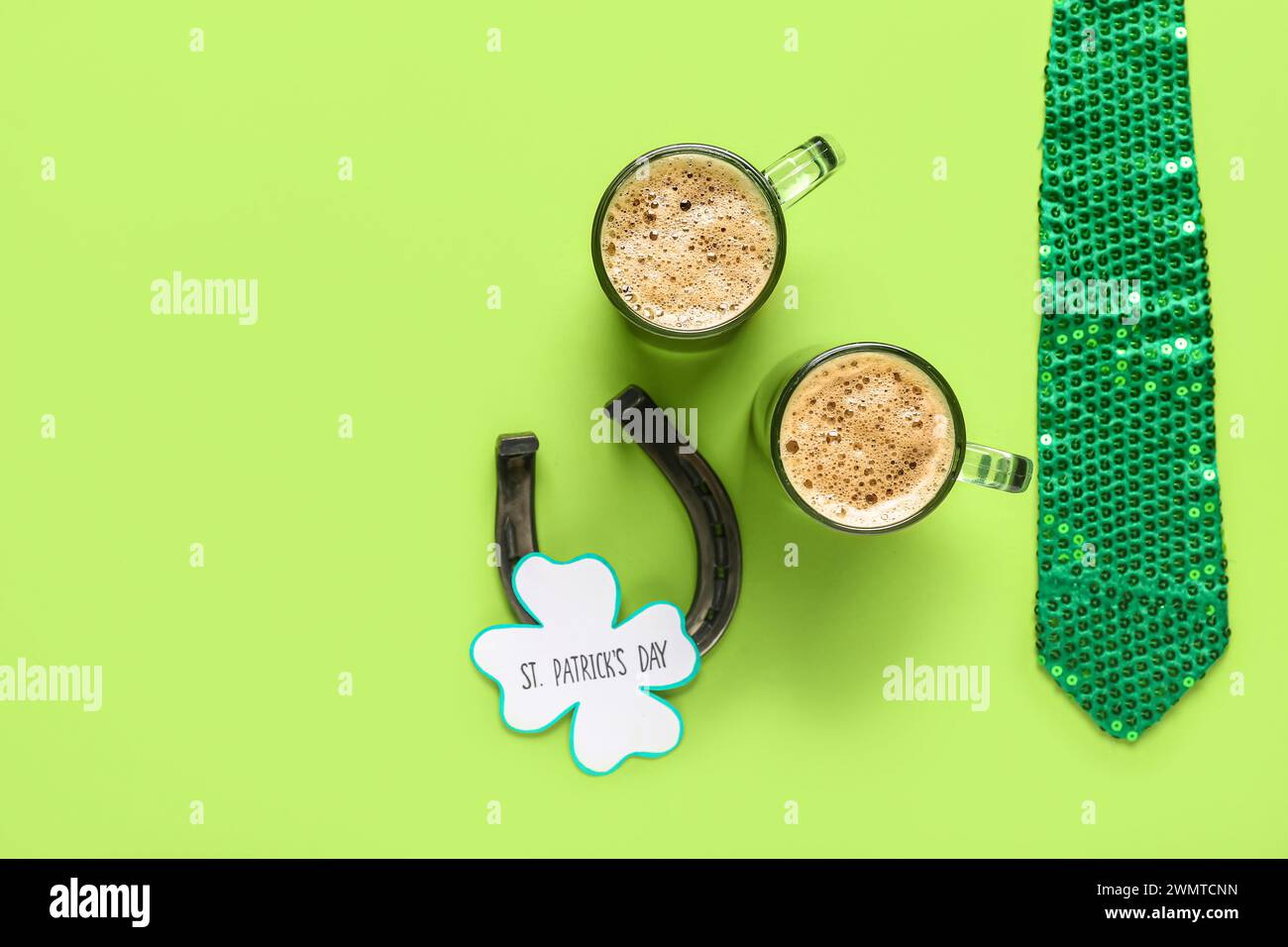Tassen mit dunklem Bier mit Hufeisen, Krawatte und festlicher Postkarte für St. Patrick's Day-Feier auf grünem Hintergrund Stockfoto