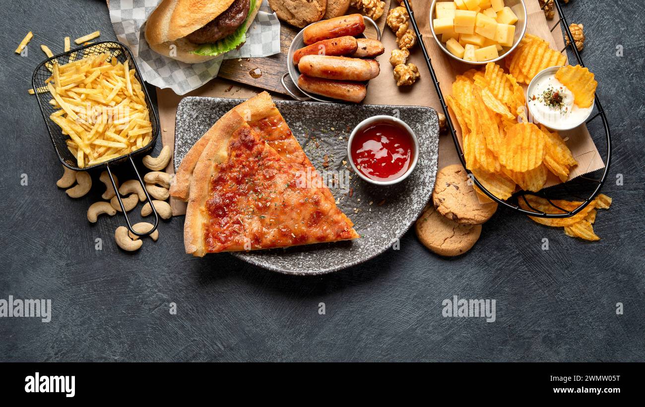 Fastfood auf dunklem Hintergrund. Junk Food für Herz und Haut. TRANS FAT-Konzept. Draufsicht, Cop-Raum Stockfoto