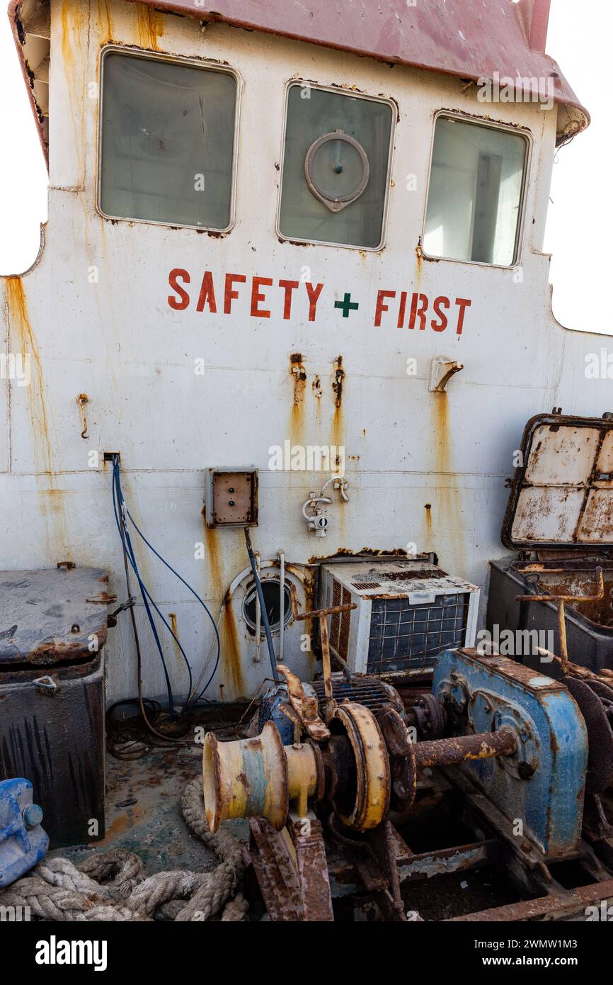 Abgerissenes und rostiges Deck eines Frachtschiffes mit alter Brücke (Radhaus), lackiert „Safety First“, Maschinen, alte Winde, an Land in den VAE gewaschen. Stockfoto