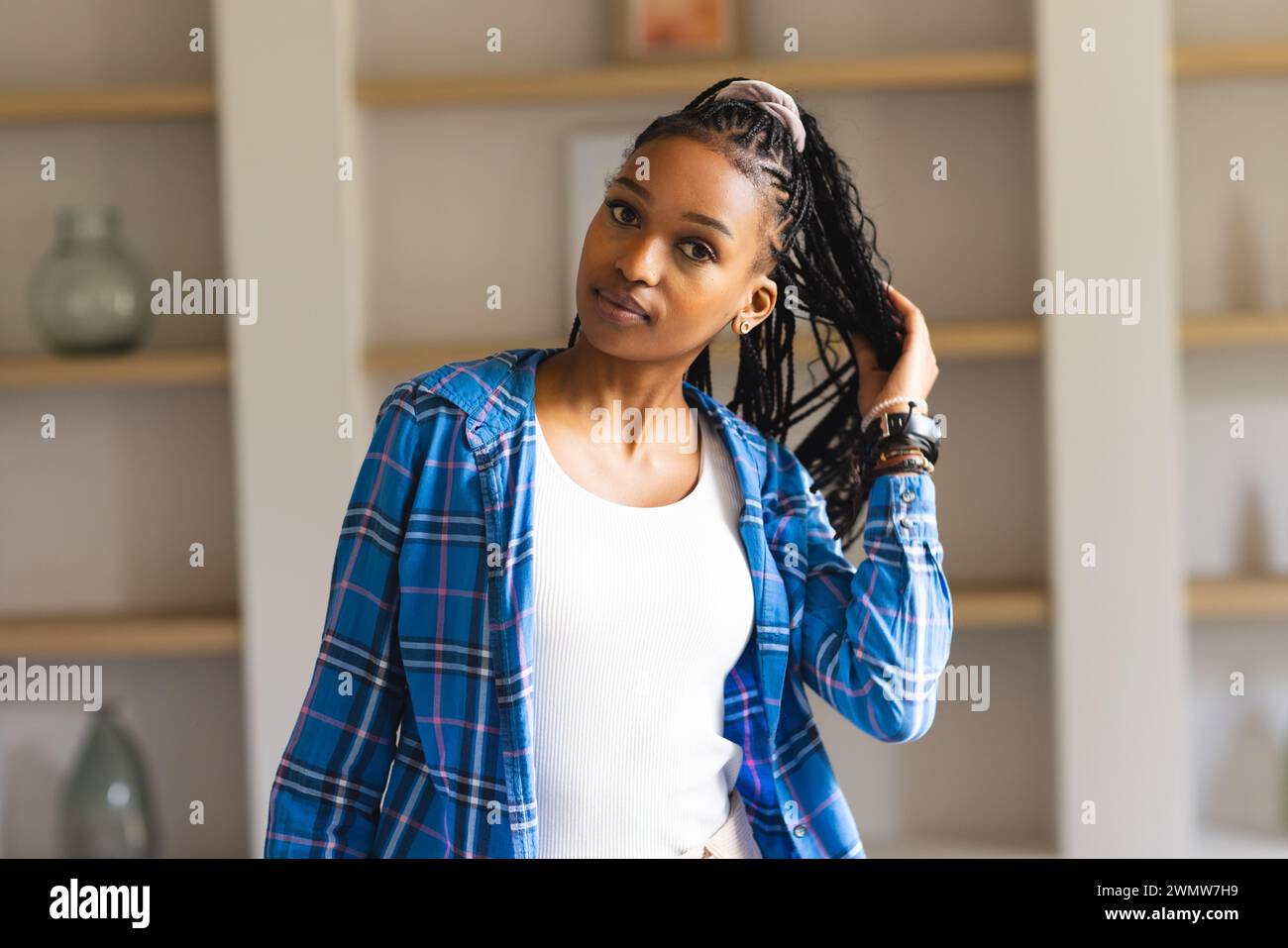 Eine junge afroamerikanische Frau posiert selbstbewusst, Hand in ihren geflochtenen Haaren Stockfoto