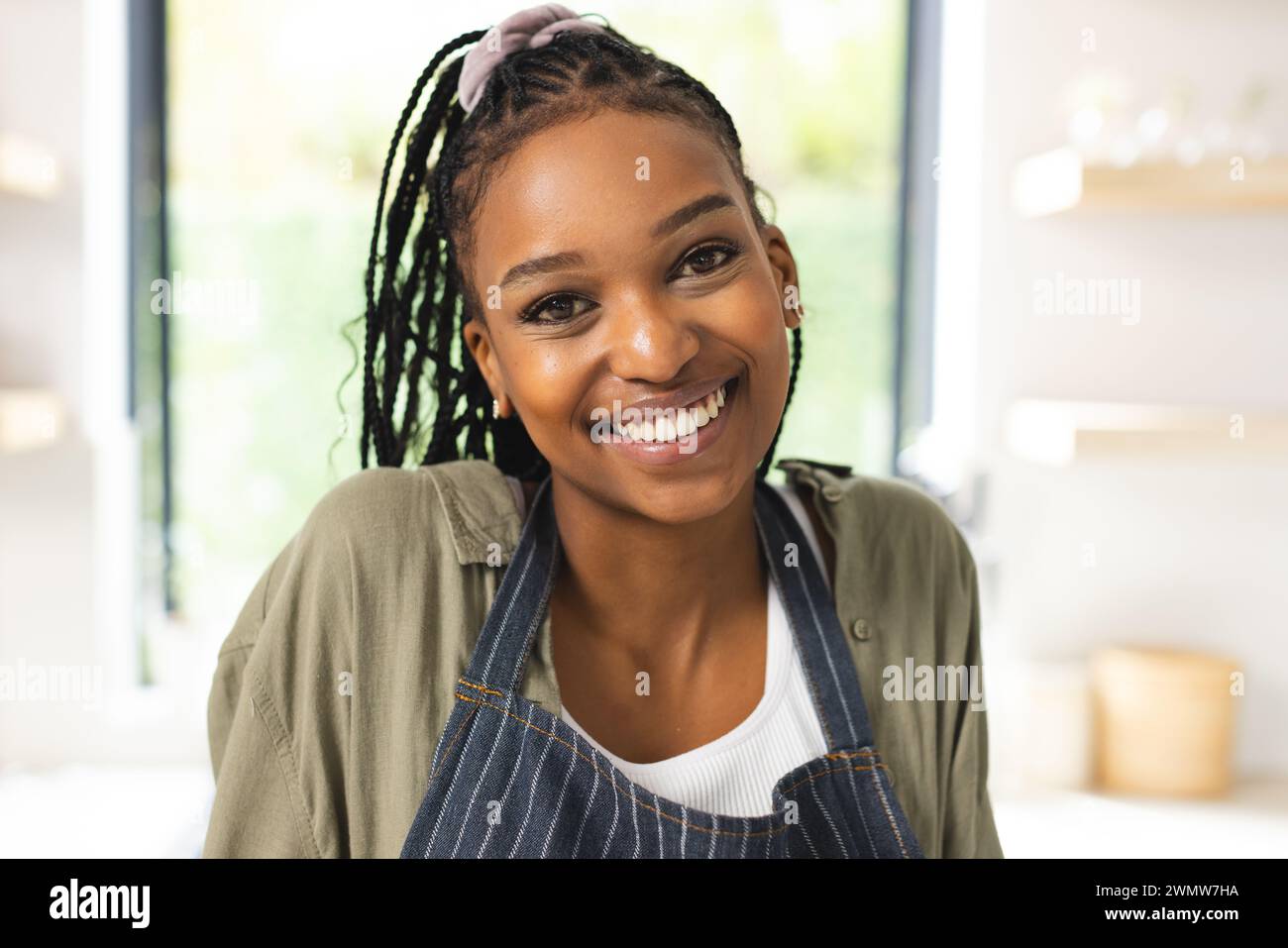 Eine junge Afroamerikanerin lächelt warm und trägt eine gestreifte Schürze Stockfoto