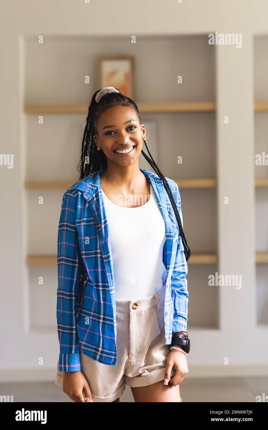 Eine junge Afroamerikanerin lächelt hell, trägt ein blaues kariertes Hemd und ein weißes Oberteil Stockfoto