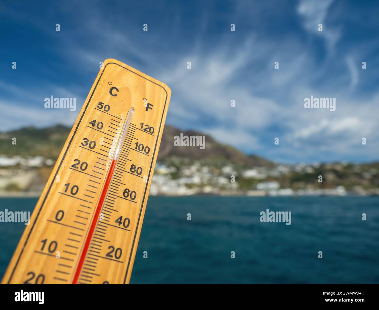 Holzthermometer mit roter Messflüssigkeit, die hohe Temperaturen an sonnigem Tag vor dem Hintergrund des Meeres anzeigt. Konzept von Urlaub, Urlaub, warmes Wetter Stockfoto