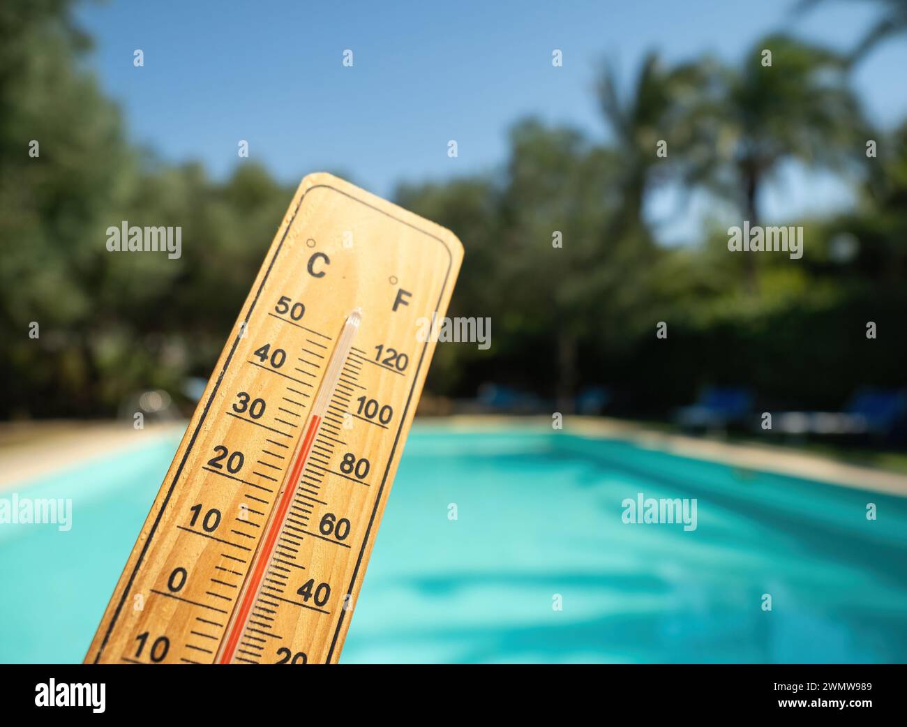 Holzthermometer mit roter Messflüssigkeit, die hohe Temperaturen an sonnigen Tagen auf dem Hintergrund des Schwimmbades anzeigt. Konzept von Urlaub, Urlaub, warm Stockfoto