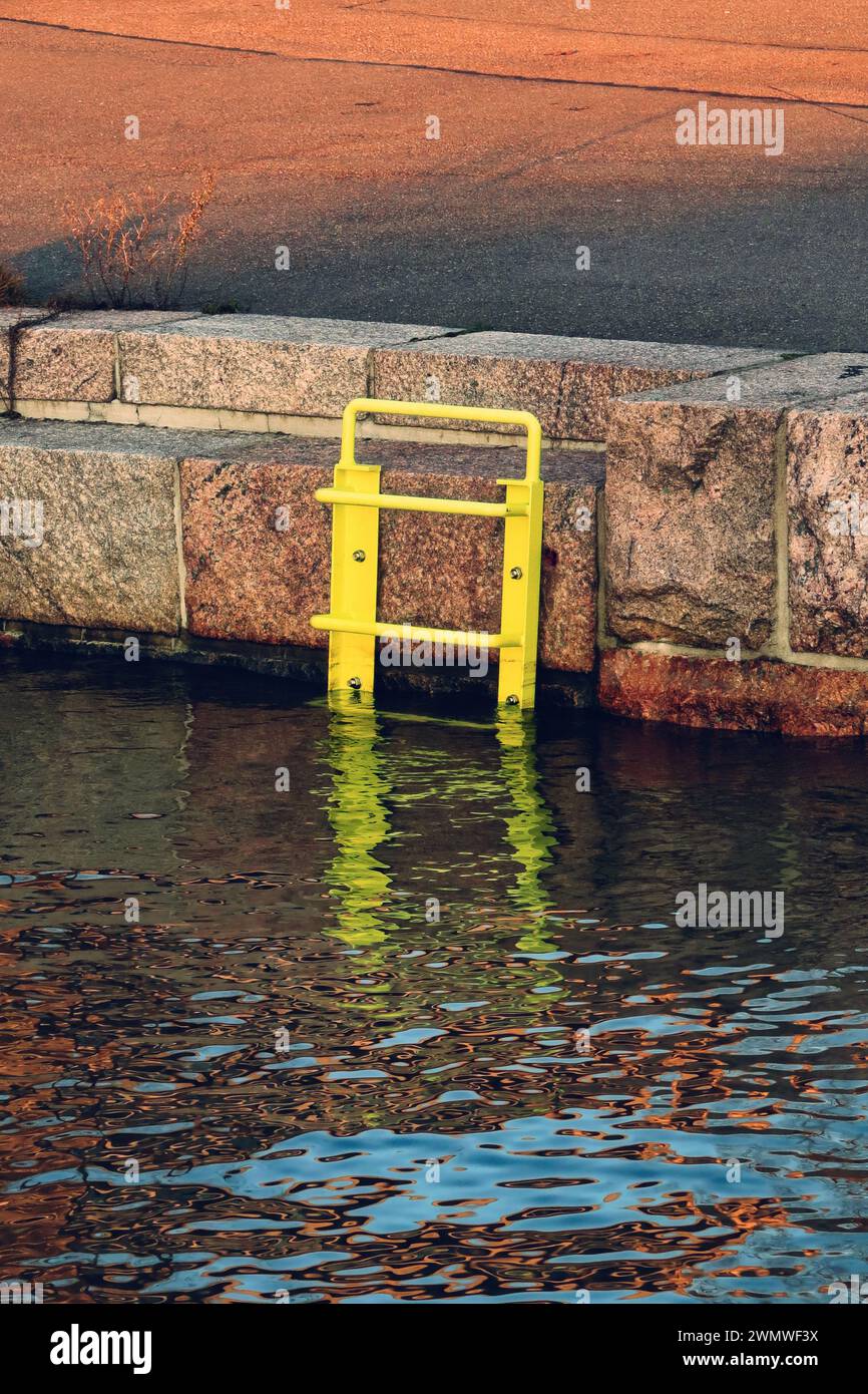 Gelbe Metallleiter am Meer, die zum Wasser führt, mit Reflexion, goldenem Stundenlicht. Stockfoto
