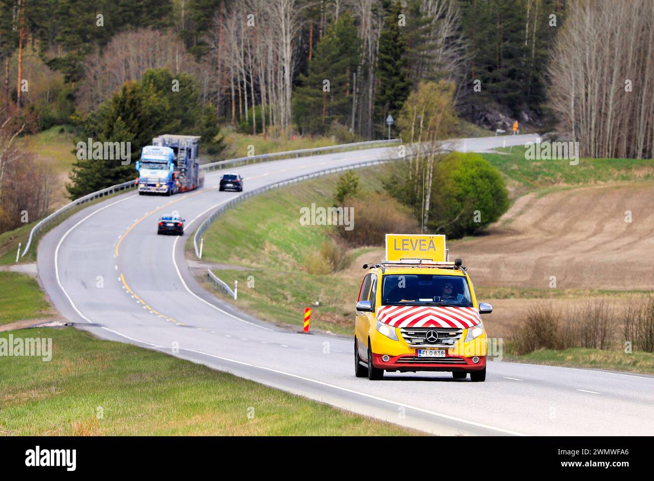 Das Pilotfahrzeug führt den Transport von Zerkleinerungsgeräten in Übergröße auf dem Highway 52 an, die Autos weichen ab. Salo, Finnland. Mai 2022. Stockfoto