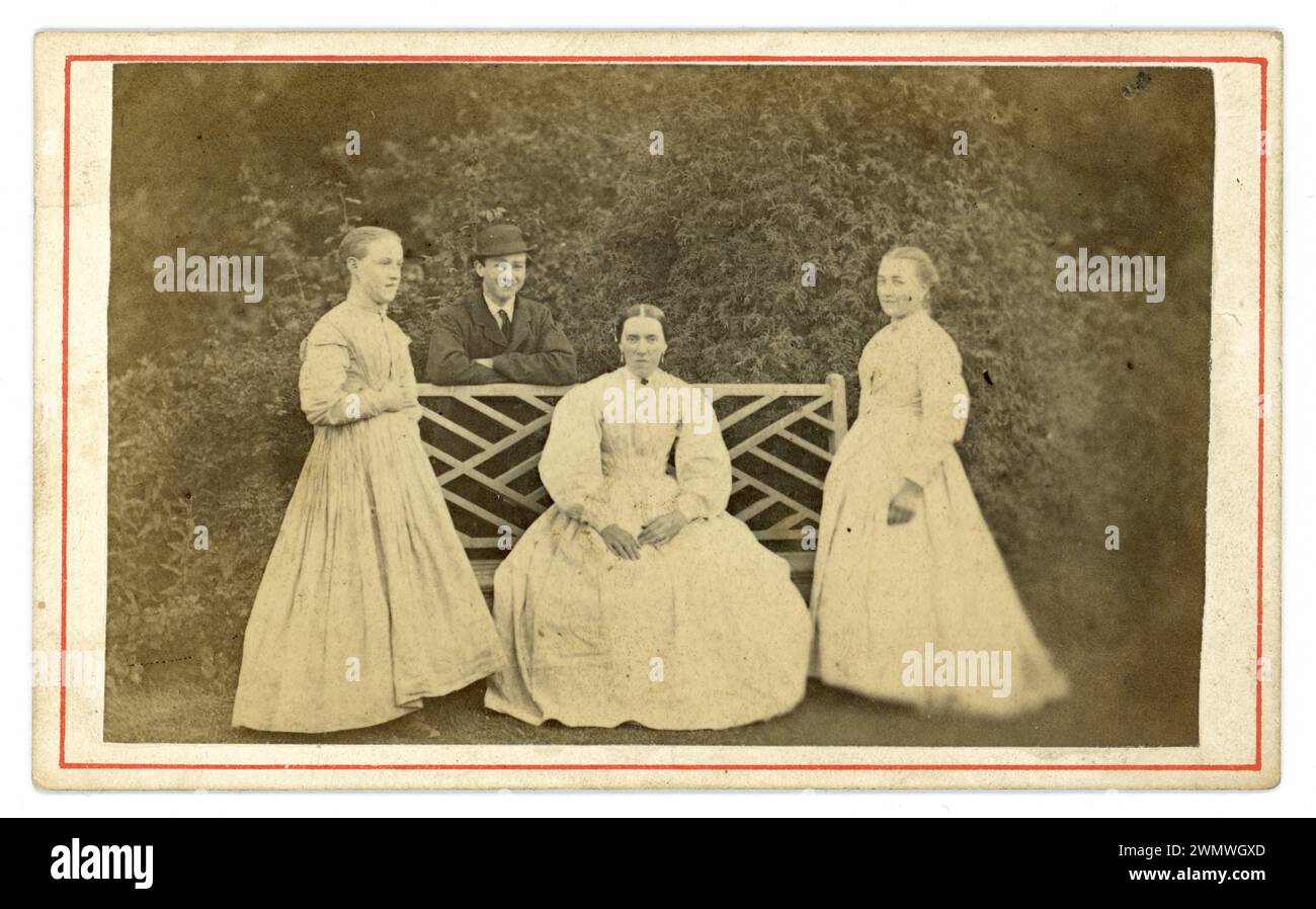 Ursprünglich Anfang bis Mitte der 1860er Jahre viktorianische Carte de Visite (Visitenkarte oder CDV) Gruppe viktorianischer Frauen draußen im Garten, schöne alte Bank, die ältere Frau sitzt auf einer Bank, lächelnder Junge im Hintergrund trägt einen Bowler Hut. Sehen Sie nicht aus wie Familienmitglieder, also vielleicht Dienstboten, Haushälterin oder Geliebte im Sitzen. Großbritannien um 1865 Stockfoto