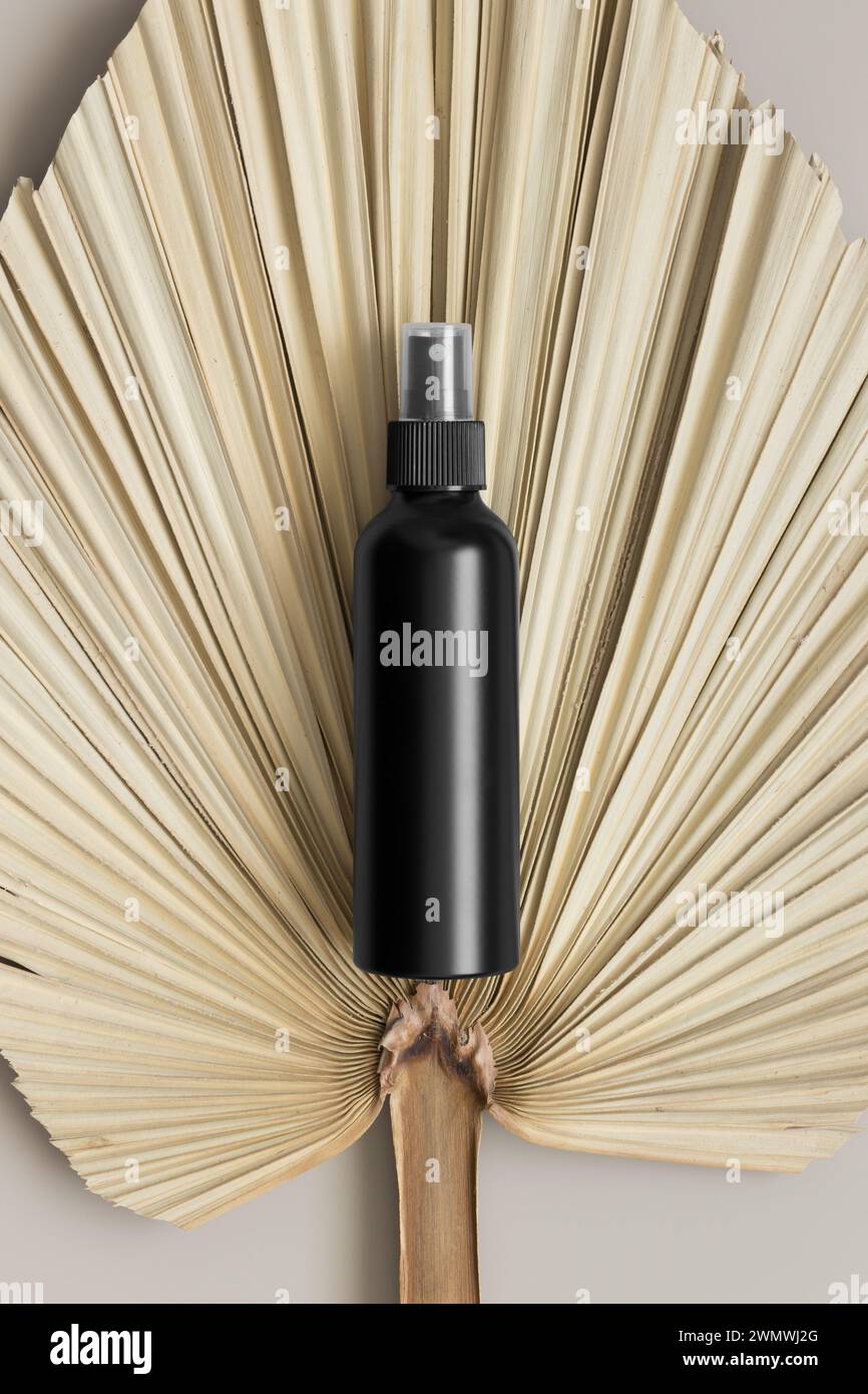 Schwarze Sprühflasche mit einem Palmblatt auf dem beigefarbenen Tisch. Stockfoto
