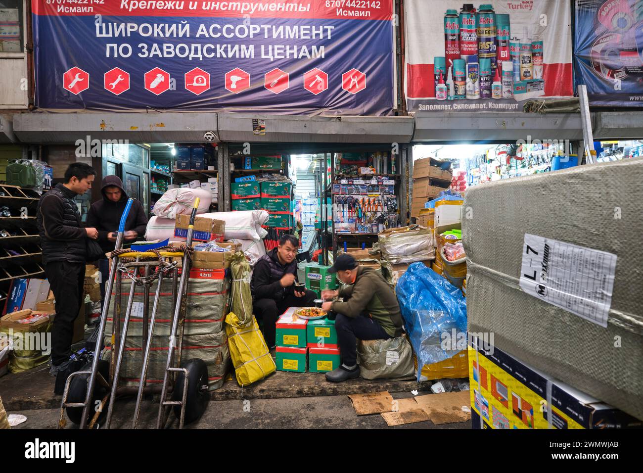 Mitarbeiter schnappen sich ein schnelles Frühstück vor ihrem Eisenwarenladen. Auf dem Barakholka Versandcontainer lokalen Markt in Almaty, Kasachstan. Stockfoto