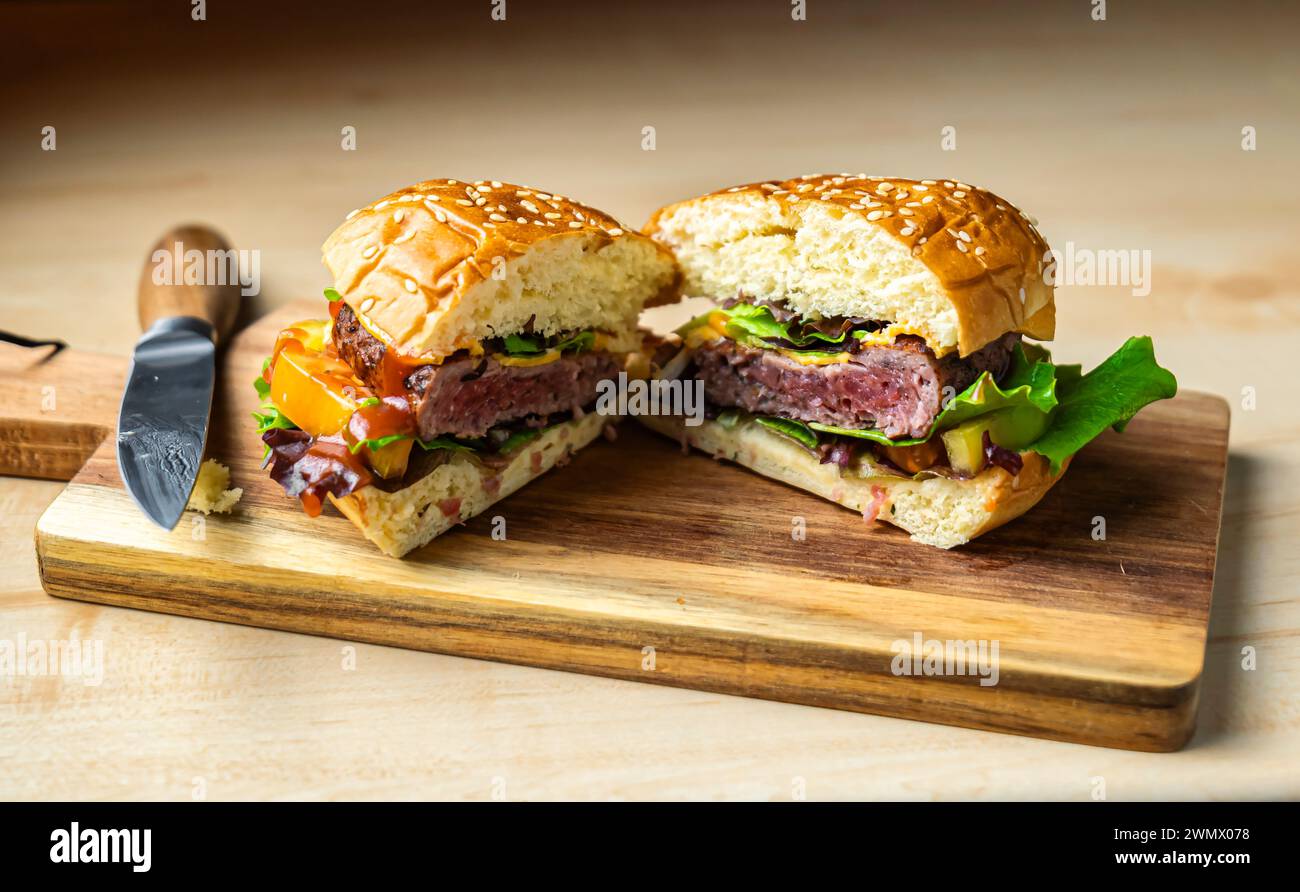 Burger wurde auf einem Holzbrett geteilt. Saftiges Fleisch, frische Tomaten, knuspriger Salat und geschmolzener Käse. Stockfoto