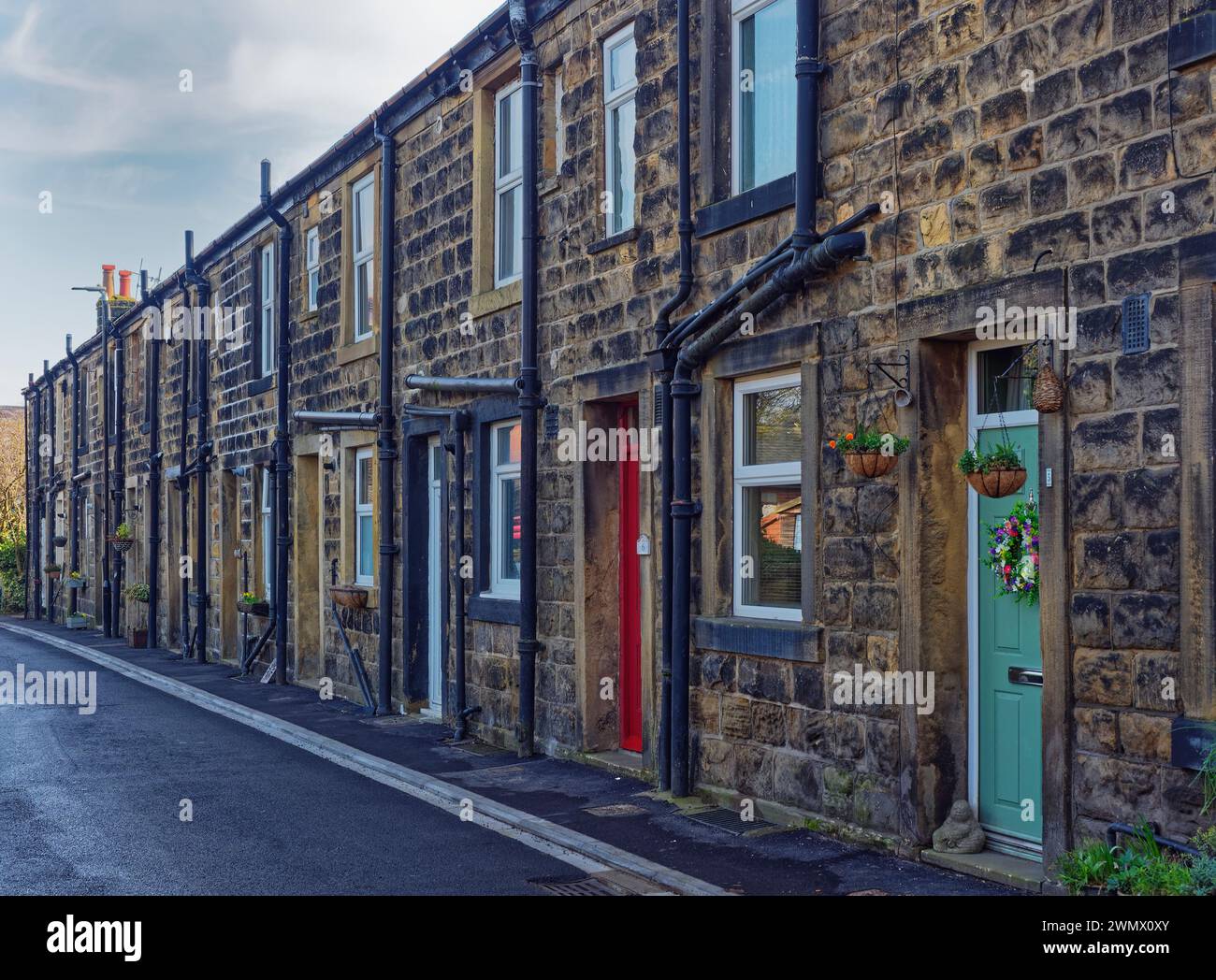 Eine Reihe traditioneller Häuser in Yorkshire an einer schmalen Straße in den Vororten von Otley, mit farbenfrohen Fronttüren und hängenden Körben. Stockfoto