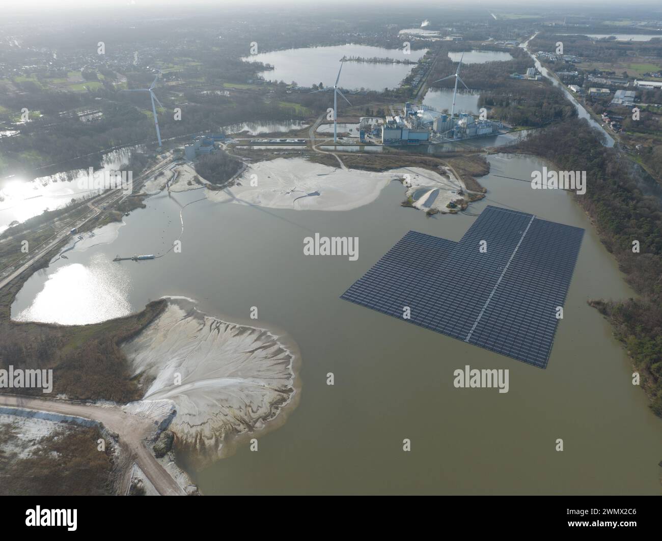 Blick auf die Drohne aus der Luft auf einen schwimmenden Solarpaneelpark neben einem großen Industriekomplex und einem Sandabbaustandort. Belgien, Europa. Stockfoto