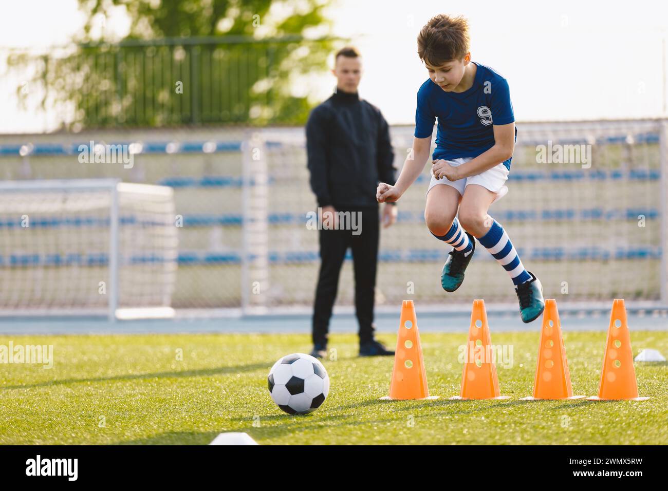 Jungen, die an Fußballtraining auf dem Schulfeld teilnehmen. Junger Mann, der Kinder in der Klasse der körperlichen Bildung betreut. Fußball-Praxis für Kinder Stockfoto