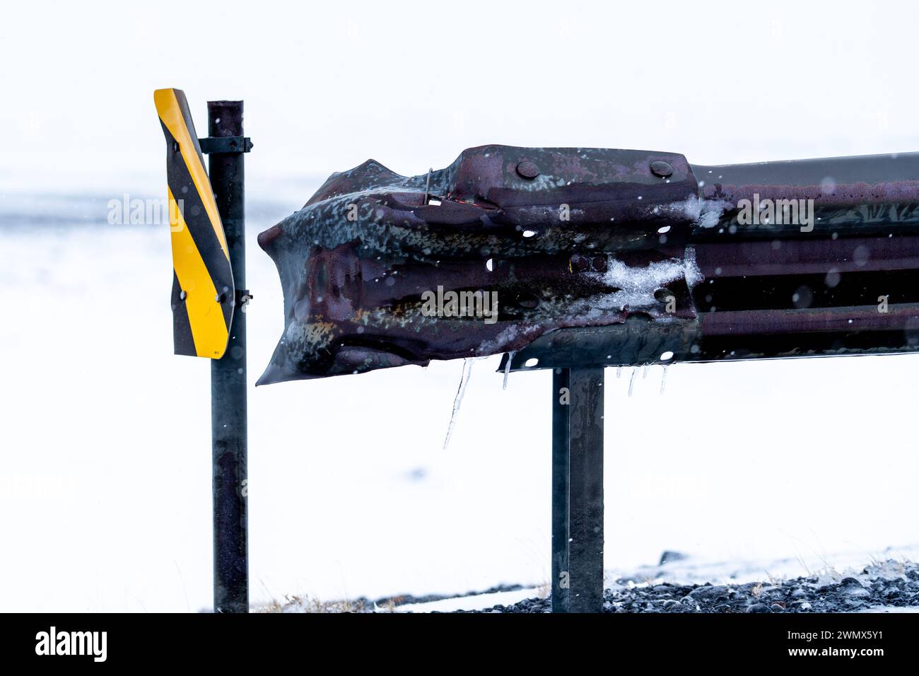 Eine vereiste Verkehrsbarriere mit einem gelben und schwarzen Straßenschild Stockfoto