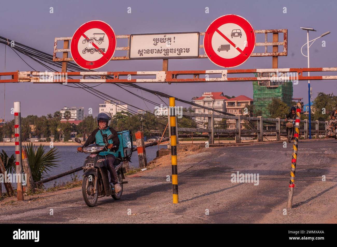 Ein Fahrer fährt mit seinem Motorrad durch den Eingang zur alten französischen Brücke auf dem Praek Tuek Chhu. Kampot, Kambodscha. © Kraig Lieb Stockfoto