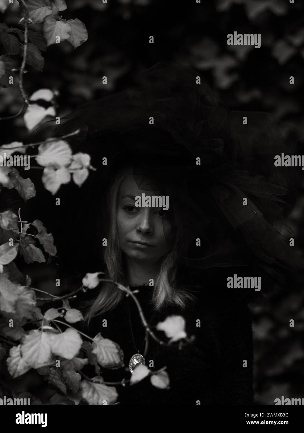 Melancholisches Schwarz-weiß-Bild des Gesichts einer Frau, teilweise verdeckt durch Hut und Blätter Stockfoto